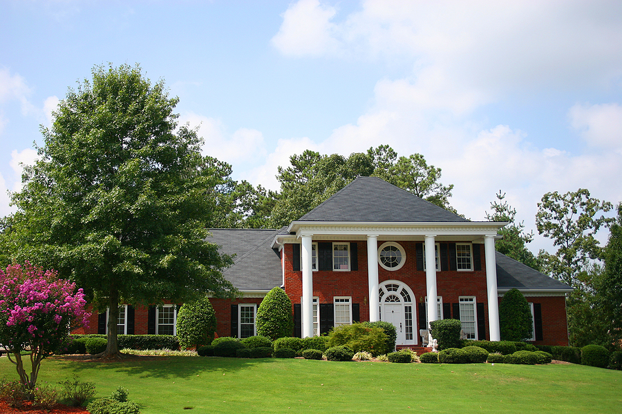 Large upscale brick house with large white porch pillars and a lush yard.
