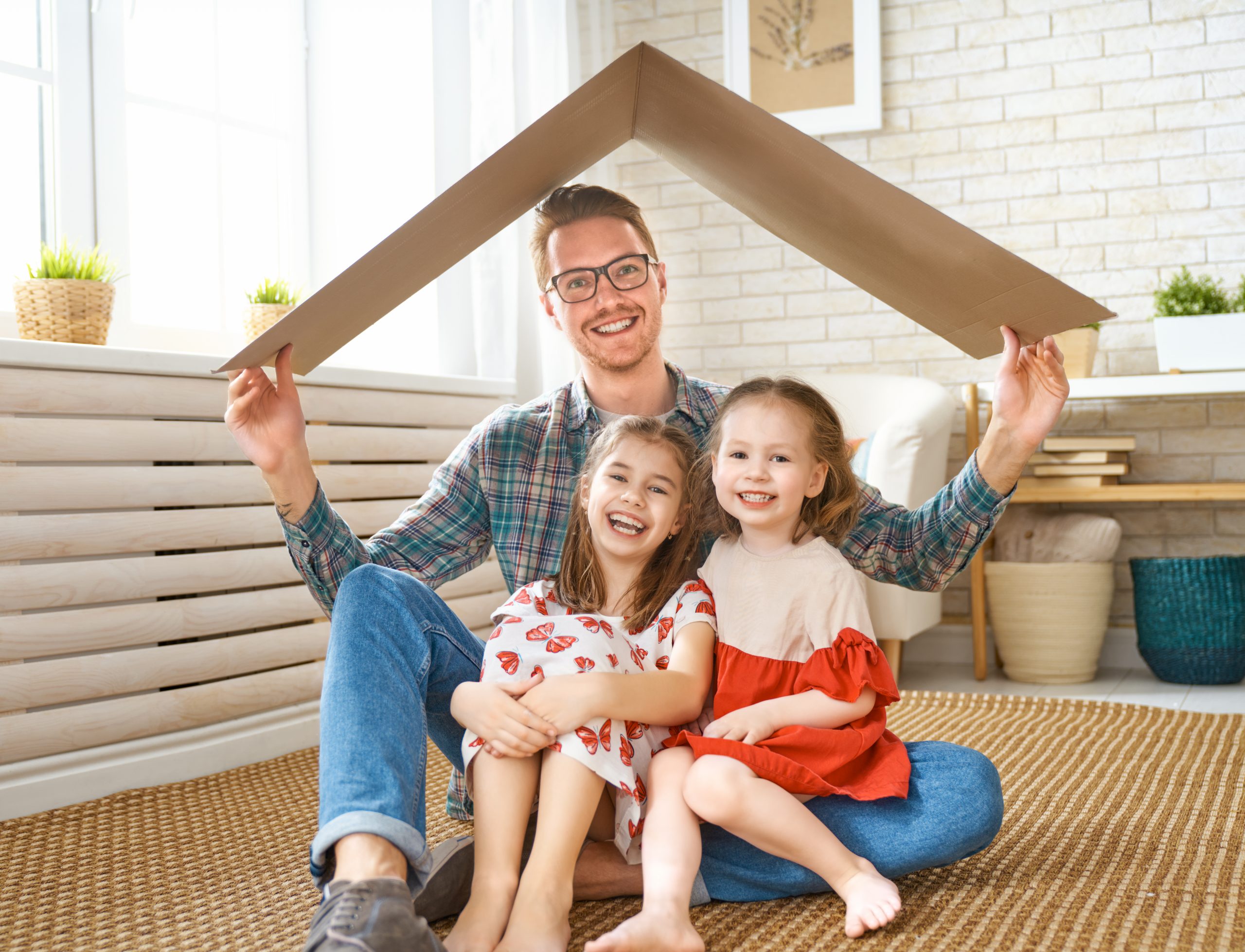 Father and two kids under a cardboard roof smiling.