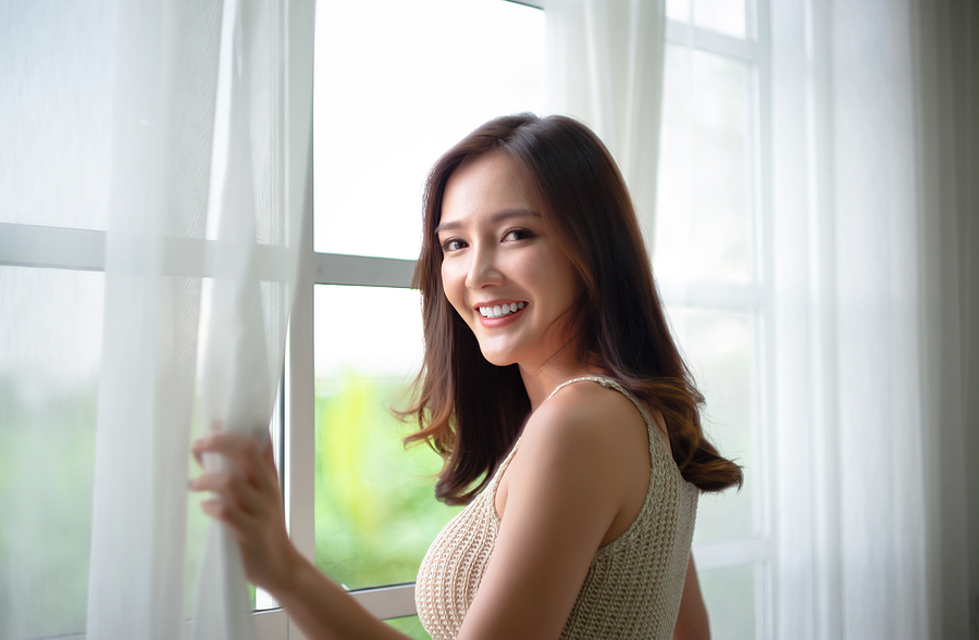 Smiling woman in front of a big window with sheer curtains.