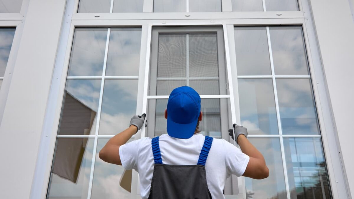 Window installer putting screen on window from exterior of home